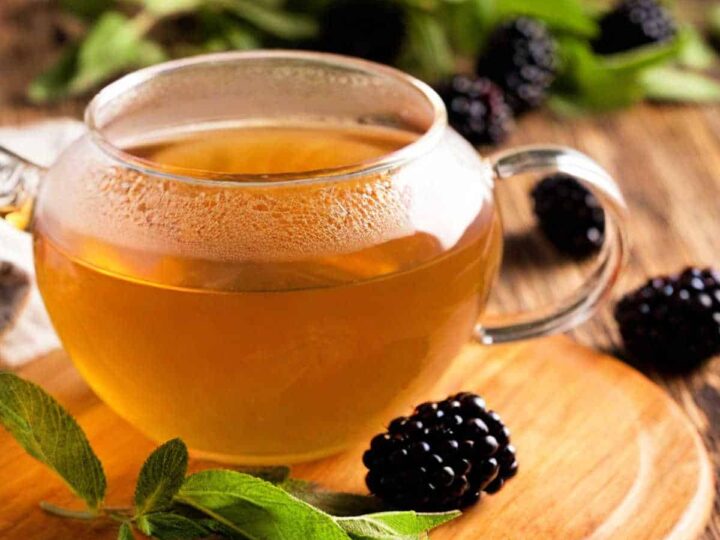 Blackberry sage tea in a glass pot with blackberries and sage leaves.