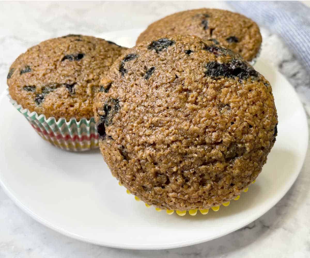 Three blueberry bran muffins on a white plate.