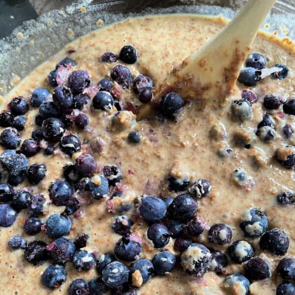 Muffin batter with blueberries in a glass bowl with a wooden spoon.