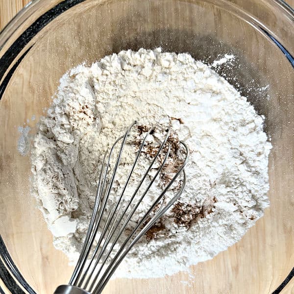 Flour and cinnamon in a glass bowl with a wire whisk.
