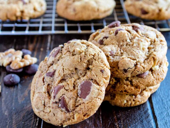 Chocolate chip cookies on a wooden board with chocolate chips and walnuts.