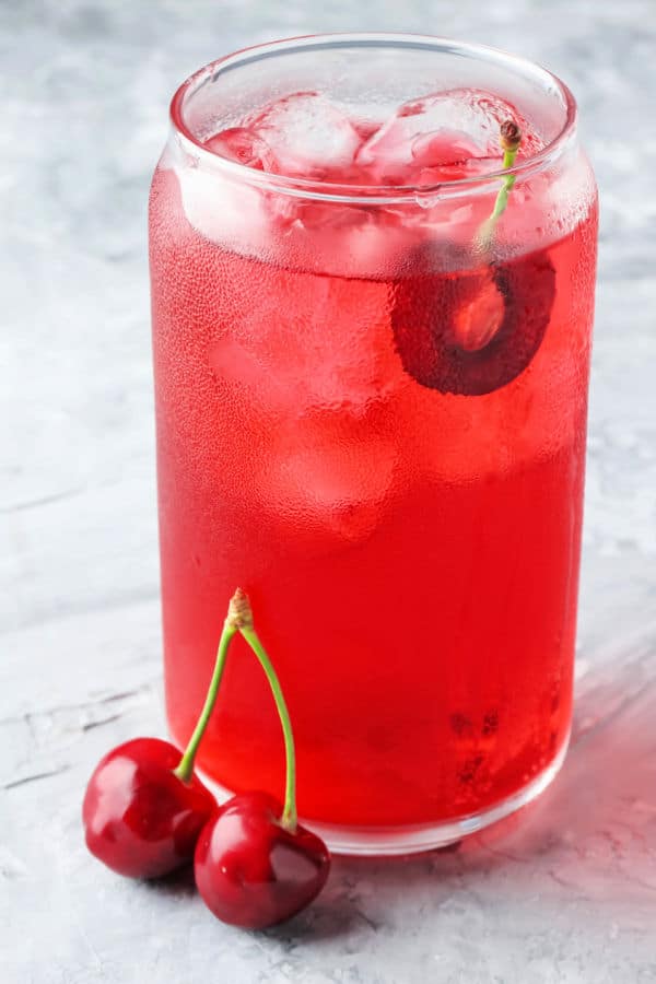 Cherry fizz in a glass garnished with cherries on a marble table.