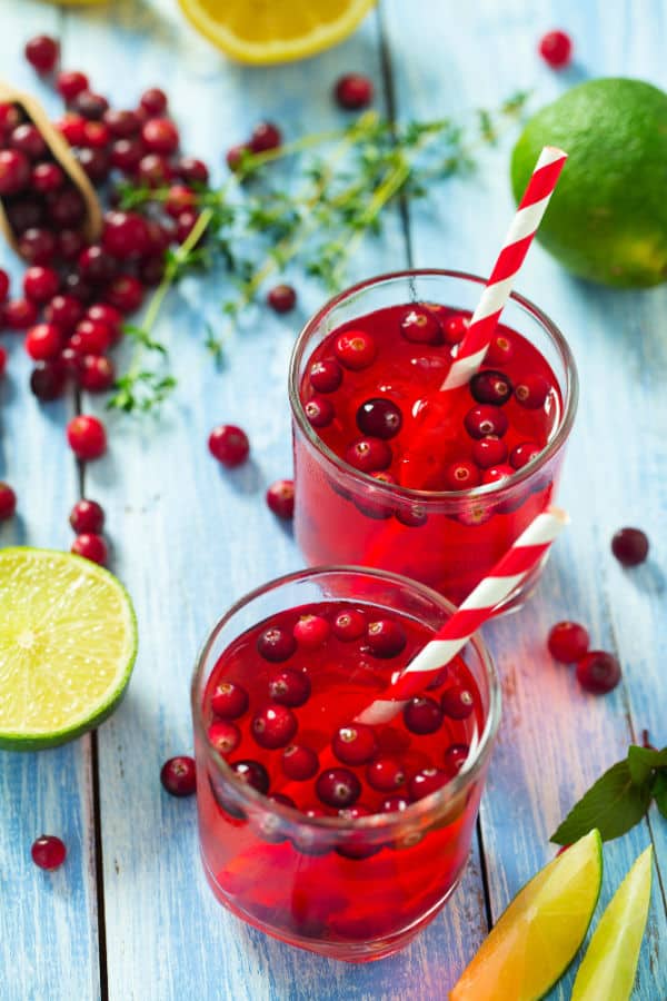 Fresh cranberry lime infused drinks with striped straws on rustic blue wood.