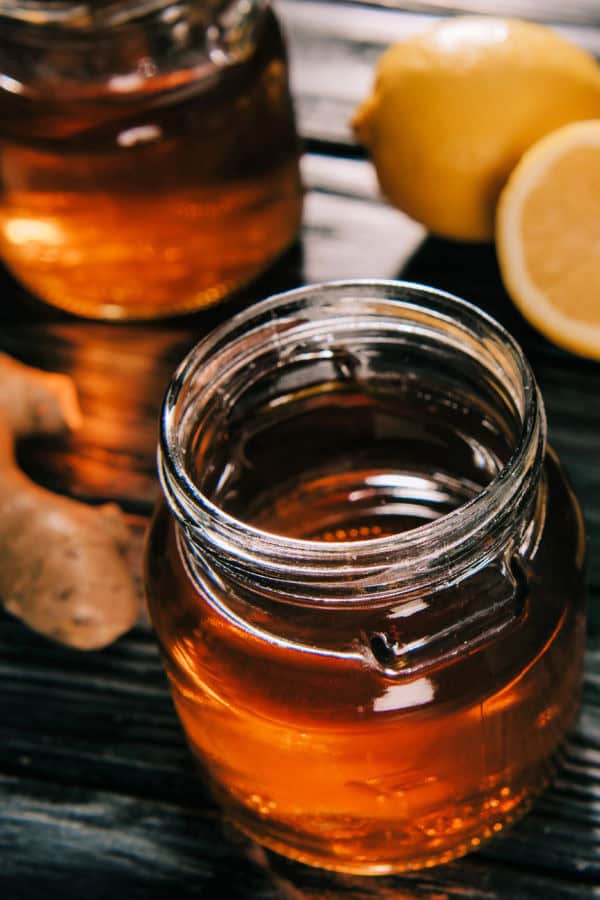 Glass jars with ginger lemon mule on a dark table with lemons and ginger.