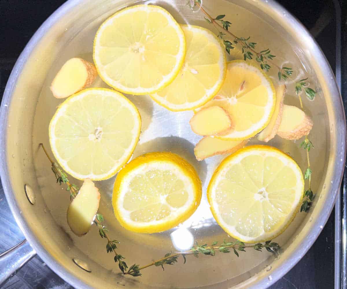 A pot with lemon slices, ginger, thyme, and water.