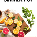 Simmer pot ingredients with citrus and herbs on a wooden board. The text reads How to make a simmer pot. Make your home smell amazing.