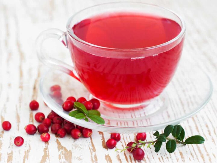 Cranberry tea in a glass cup and saucer with fresh cranberries.