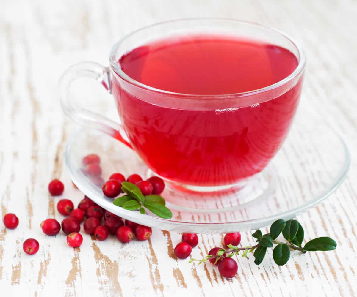 Cranberry tea in a glass cup and saucer with fresh cranberries.