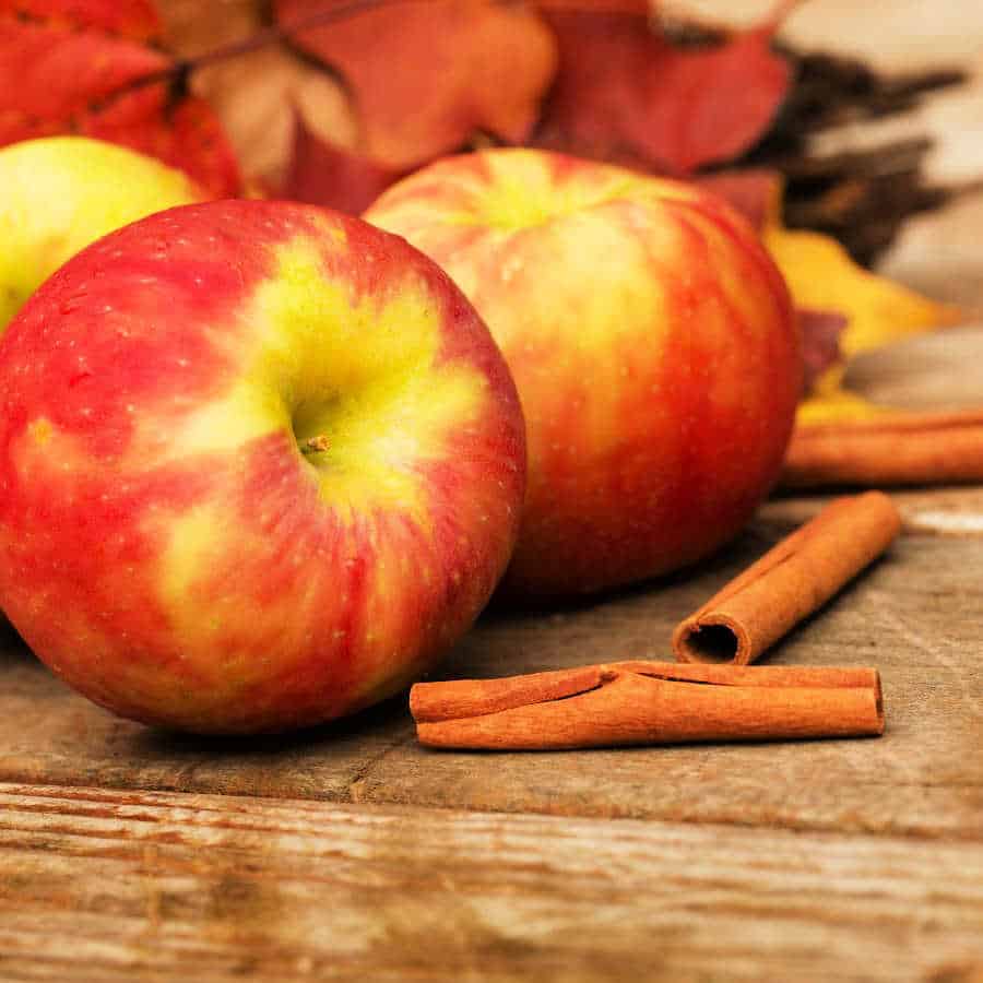 Apples and cinnamon sticks on a wooden table.