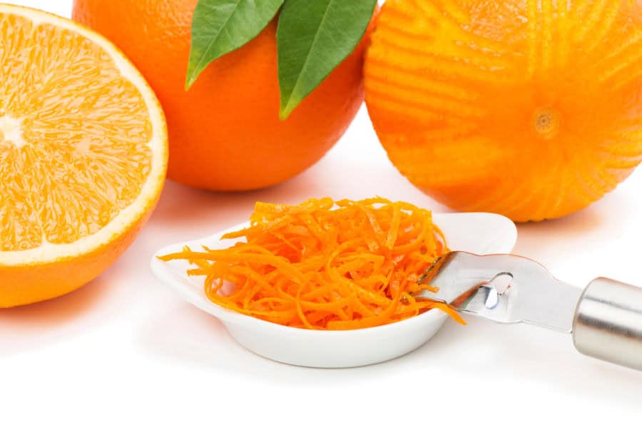 Oranges and orange zest in a small white bowl with a zester.