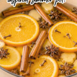 Cinnamon sticks, cloves, star anise and orange slices in a pot on a wooden table. The text reads pumpkin spice inspired simmer pot!