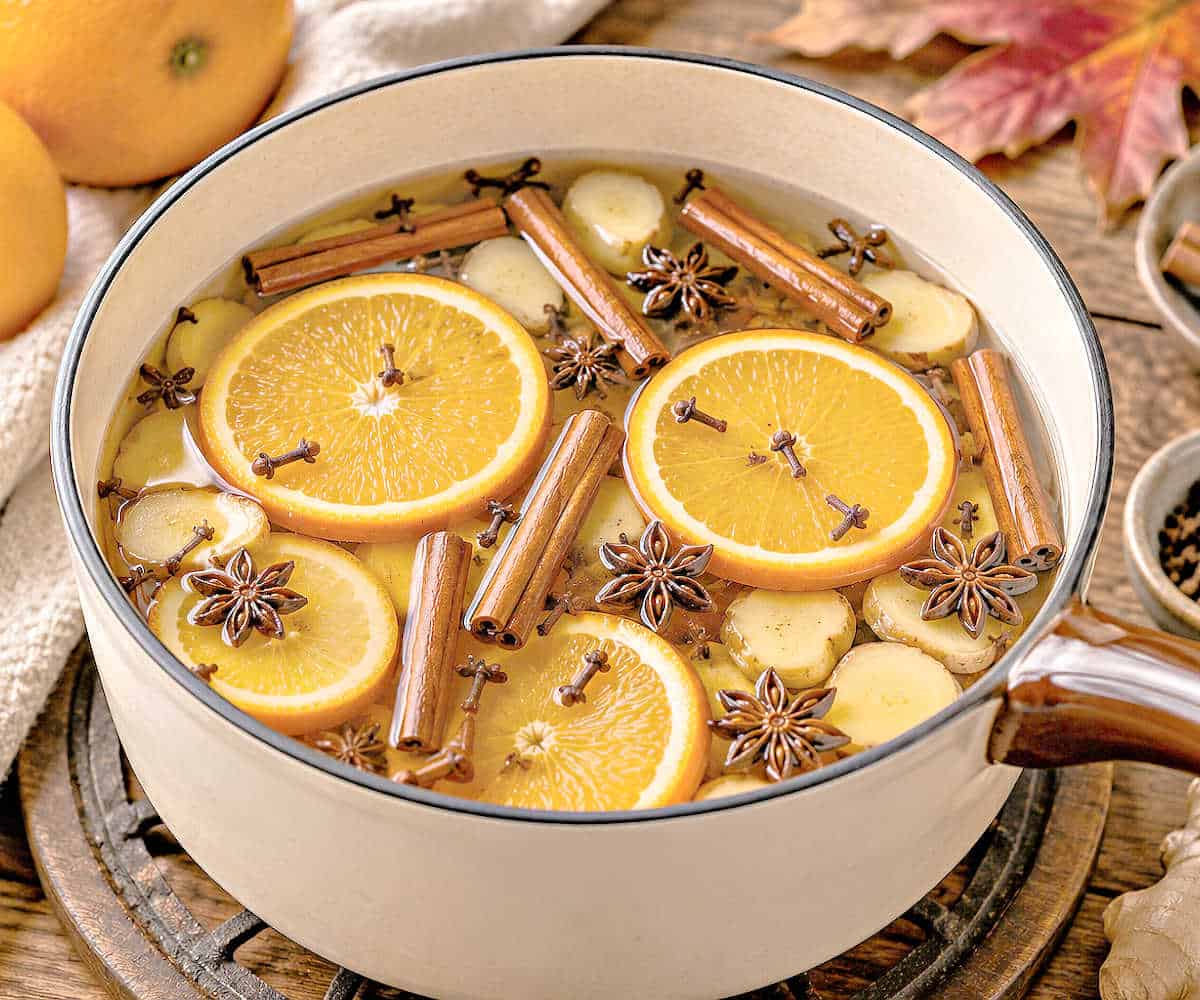 Cinnamon sticks, cloves, star anise and orange slices in a pot on a wooden table.