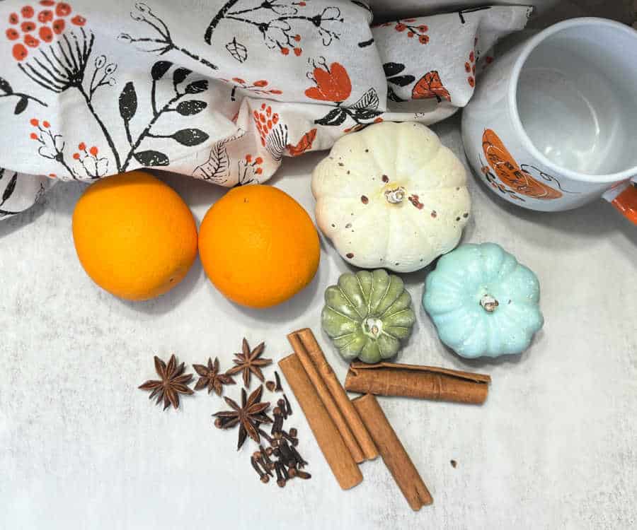 Fall spices, oranges, and colourful plastic pumpkins on a table with a fall themed tea towel and orange and white mug.