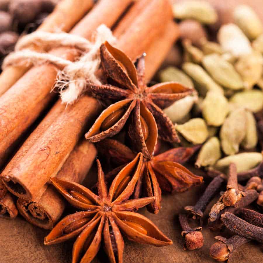 Cinnamon sticks, star anise, cloves, and cardamom pods on a brown table.