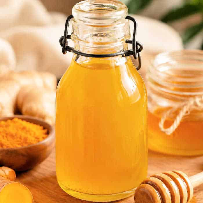 Turmeric and Honey simple syrup in a glass jar on a table with turmeric, ginger and honey.