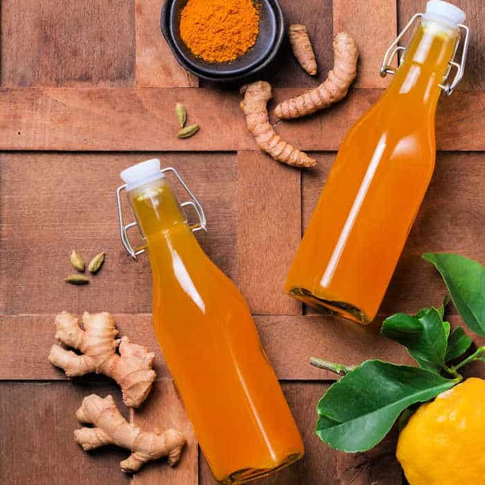 Two glass jars of turmeric and honey simple syrup on a wooden board with turmeric, ginger, and lemon.