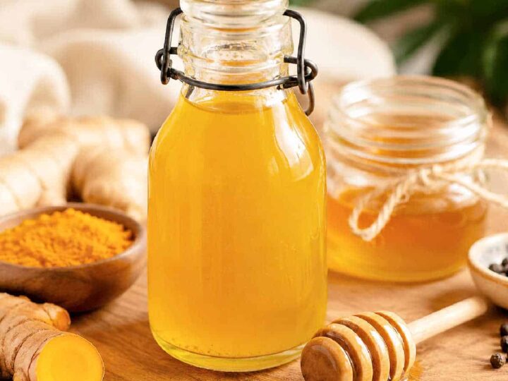 Turmeric and Honey simple syrup in a glass jar on a table with turmeric, ginger and honey.